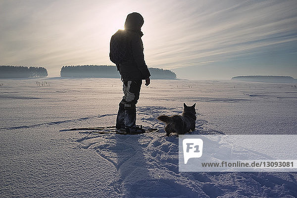 Rückansicht eines Mannes mit Hund auf schneebedecktem Feld gegen den Himmel stehend