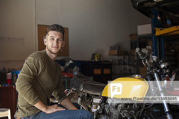 Porträt eines selbstbewussten Mannes  der mit dem Motorrad in der Garage sitzt