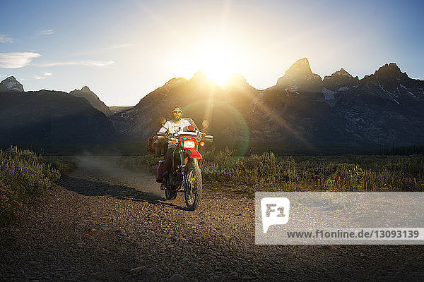 Man riding motorcycle on dirt road against mountains