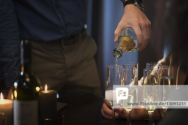 Midsection of man pouring champagne in glasses