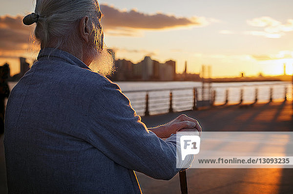 Senior man sitting on promenade at sunset