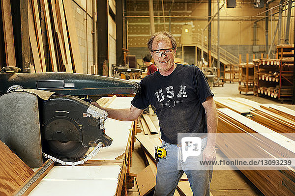 Portrait of smiling carpenter by machinery at workshop
