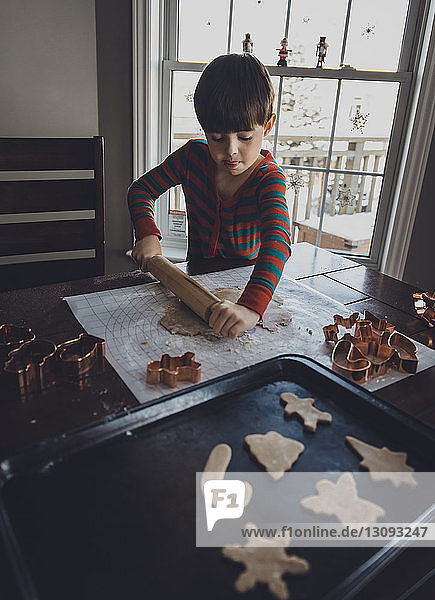 Junge rollt zu Weihnachten zu Hause Keksteig auf den Tisch