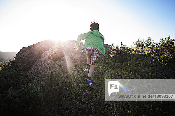 Rückansicht eines Jungen  der an einem sonnigen Tag auf einem Grasfeld läuft