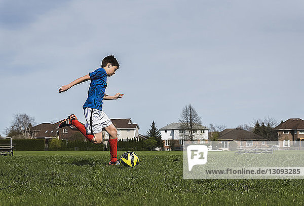 Seitenansicht eines Jungen  der beim Spielen auf einem Rasenplatz einen Fussball kickt