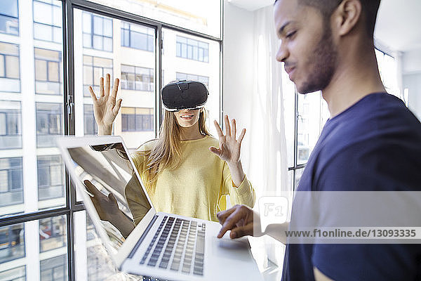 Businesswoman examining virtual reality simulator while male colleague using laptop