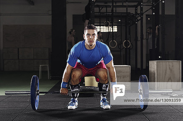 Portrait of determined male athlete lifting barbell in gym
