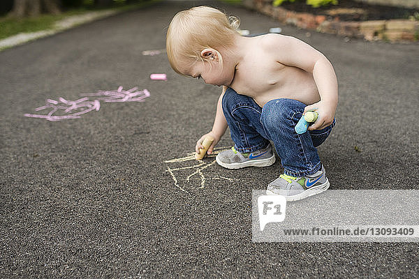 Shirtless boy writing with chalk on footpath
