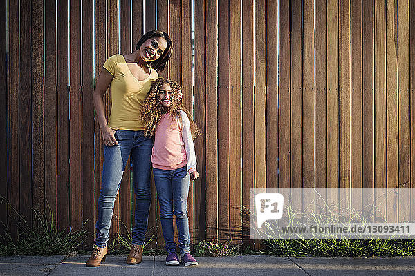 Porträt einer glücklichen Mutter und Tochter an einem Holzzaun stehend