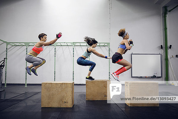 Side view of determined female athletes doing box jumping at health club