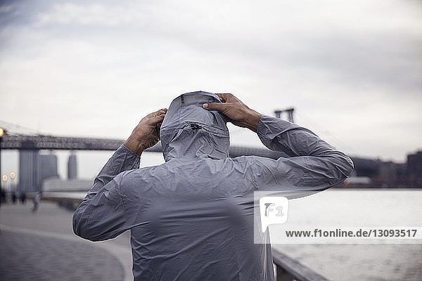 Rear view of male athlete wearing hooded jacket with Williamsburg Bridge in background