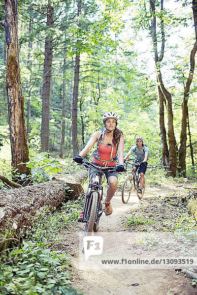 Couple riding bicycle on dirt road in forest