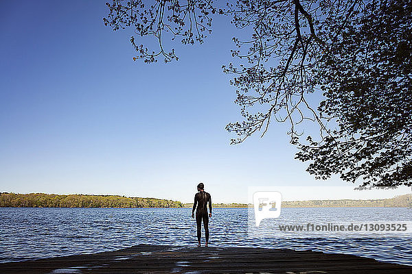 Rückansicht einer Schwimmerin  die auf einer Strandpromenade am See vor klarem blauen Himmel steht