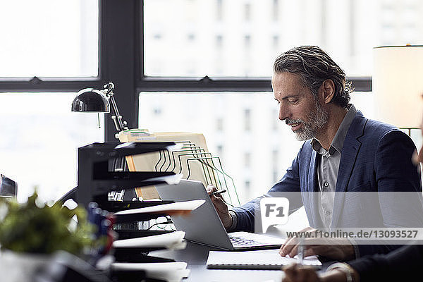 Businessman working on laptop computer against window in office