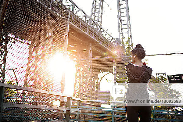 Rückansicht einer Frau  die sich an einem sonnigen Tag gegen die Williamsburg Bridge streckt