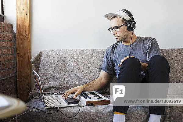 Mann hört Musik  während er einen Laptop-Computer auf dem Sofa benutzt