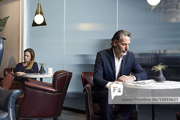 Geschäftsmann liest Buch  während eine Geschäftsfrau ein Smartphone in der Cafeteria des Kreativbüros benutzt
