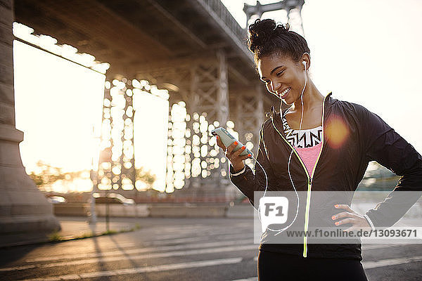 Glückliche Joggerin benutzt Telefon  während sie auf der Straße steht