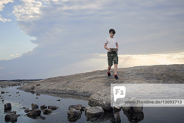 Boy carrying rocks while walking on Arabia Mountain against cloudy sky