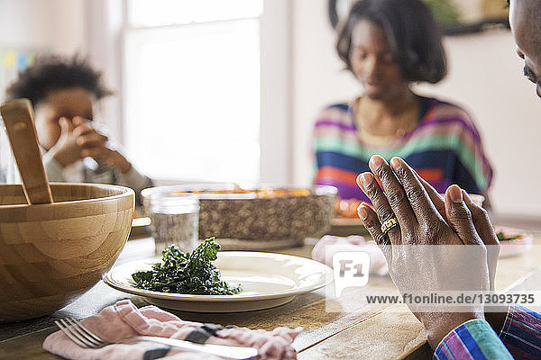 Ausgeschnittenes Bild einer Familie  die am Esstisch das Tischgebet spricht