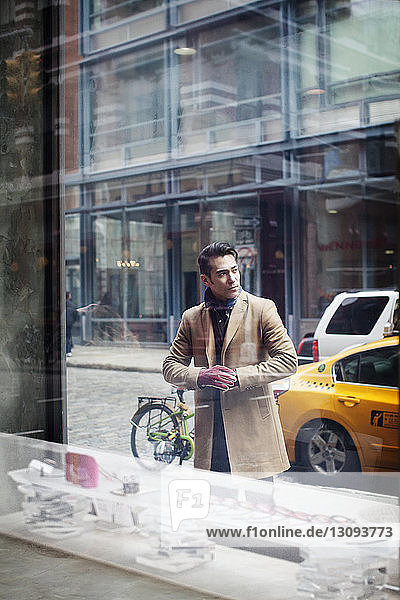 Mann steht auf Fußweg  gesehen durch Fenster im Laden