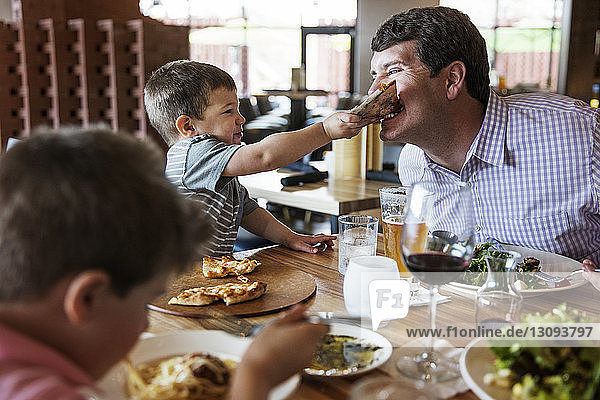 Boy feeding pizza to father in restaurant