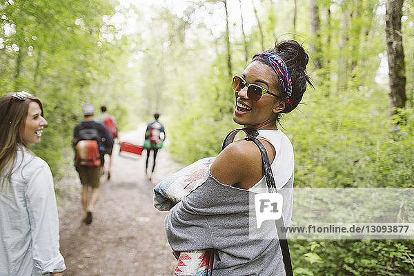 Freunde mit Rucksack wandern auf Feldweg zwischen Bäumen im Wald