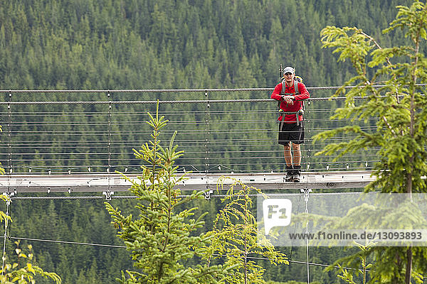 Hiker with backpack standing on footbridge amidst forest