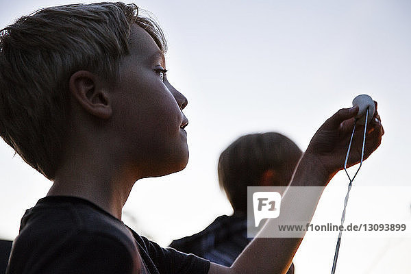 Low angle view of boy putting marshmallow on skewer against sky