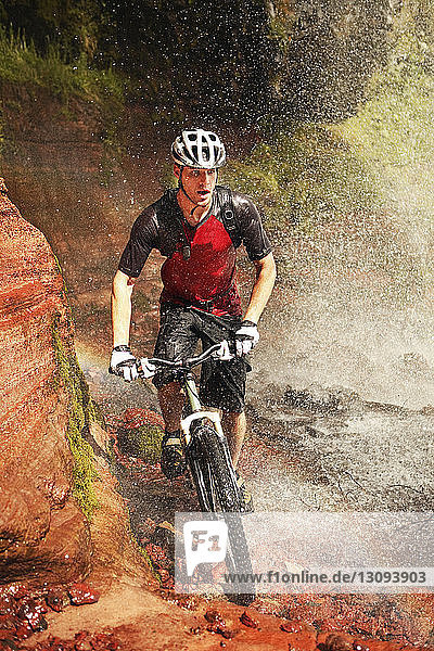 Wet young man cycling by waterfall