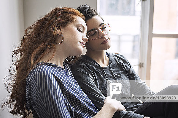 Lesbian couple sitting on chair by window at home