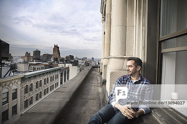 Man sitting on balcony against cityscape