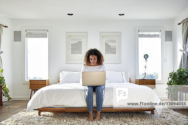 Woman using laptop computer while sitting on bed at home