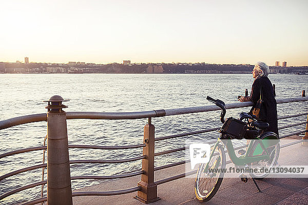 Ältere Frau mit Blick aufs Meer  während sie auf der Promenade mit dem Fahrrad steht