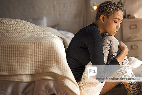 Seitenansicht einer traurigen Frau  die im Schlafzimmer auf dem Boden sitzt