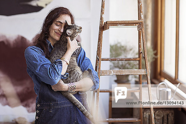 Lächelnder Künstler umarmt Katze  während er im Workshop steht