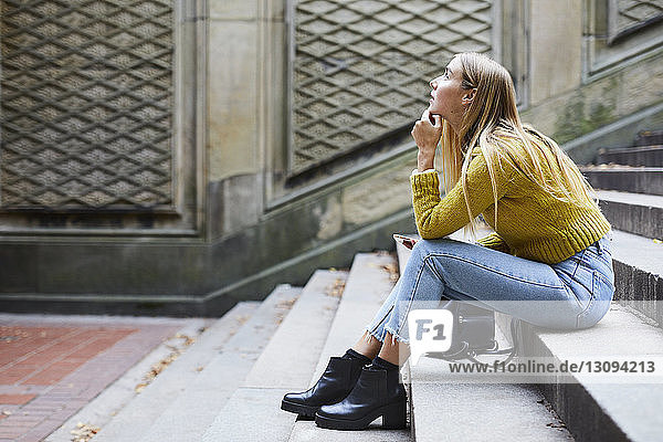 Seitenansicht einer nachdenklichen Frau  die auf Stufen im Park sitzt