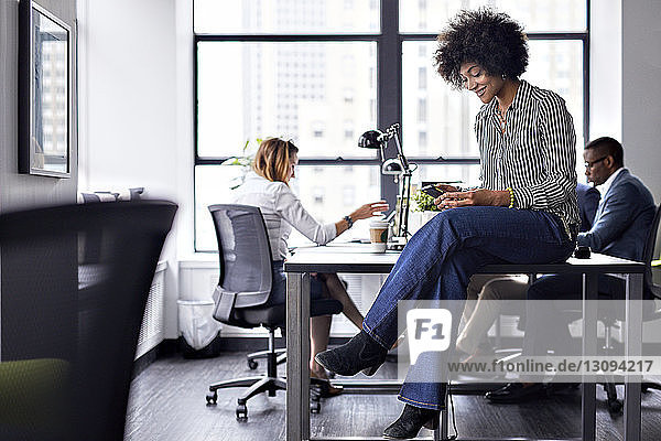 Geschäftsfrau benutzt Smartphone  während Kollegen im Hintergrund arbeiten