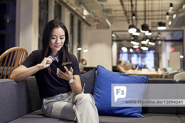 Confident entrepreneur using mobile phone while sitting on sofa at creative office