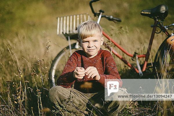 Porträt eines Jungen  der auf dem Feld gegen ein Fahrrad kauert