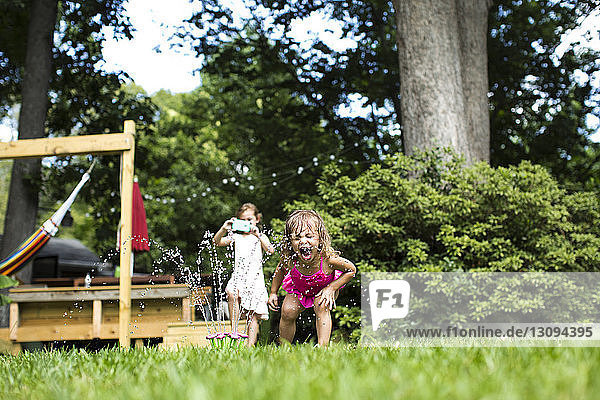 Mädchen fotografiert  während die Schwester im Garten mit der Sprinkleranlage spielt