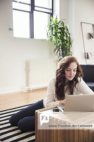 Geschäftsfrau benutzt Laptop  während sie im Büro auf einem Teppich sitzt