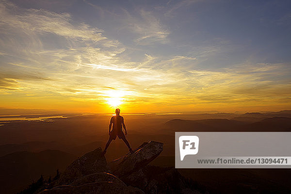 Full length of hiker standing on top of mountain against sky during sunset