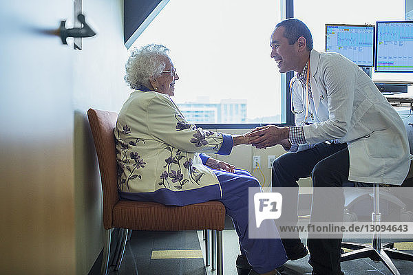 Lächelnder männlicher Arzt hält Hand  während er mit Patient auf der Krankenhausstation spricht