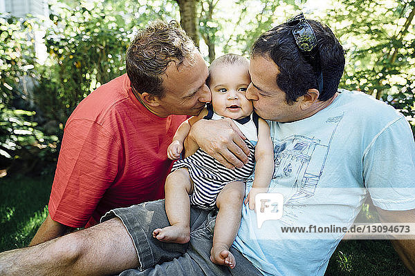 Homosexuelles Paar küsst Baby  während es im Hinterhof sitzt