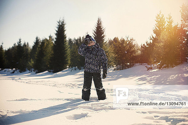Boy standing on snow covered field against sky during sunset