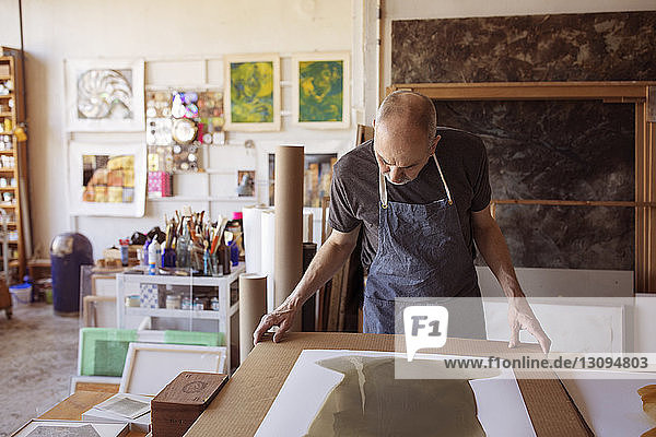 Senior artist looking painting at table in workshop