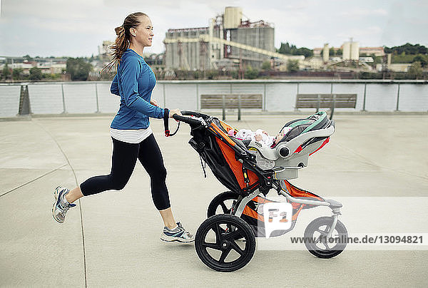 Side view of woman pushing baby stroller while jogging in city