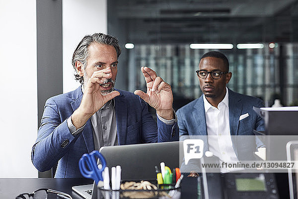 Businessman looking at male colleague gesturing in office