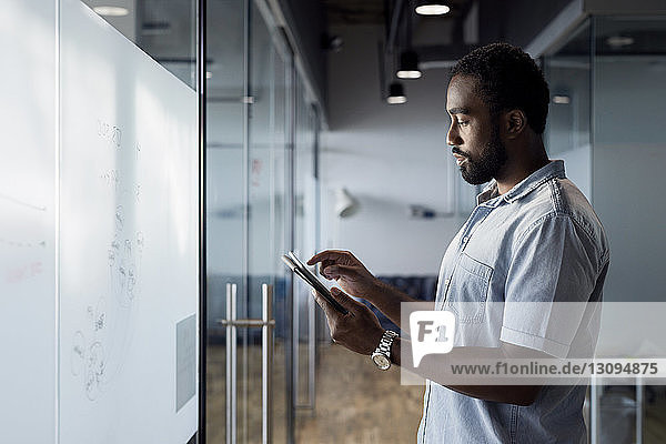 Seitenansicht eines Geschäftsmannes  der ein digitales Tablet benutzt  während er im Bürokorridor steht